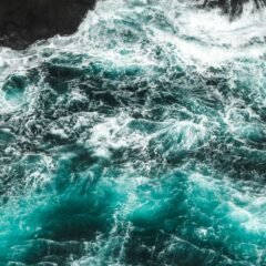 Бурхливі хвилі з білою піною біля темного скелястого берега, вид згори