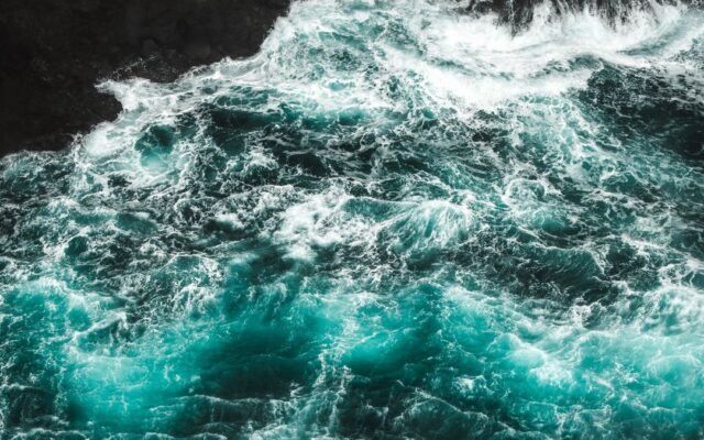 Бурхливі хвилі з білою піною біля темного скелястого берега, вид згори