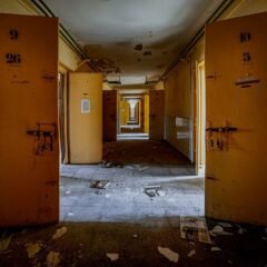 Порожній коридор покинутої будівлі з відчиненими металевими дверима й уламками на підлозі