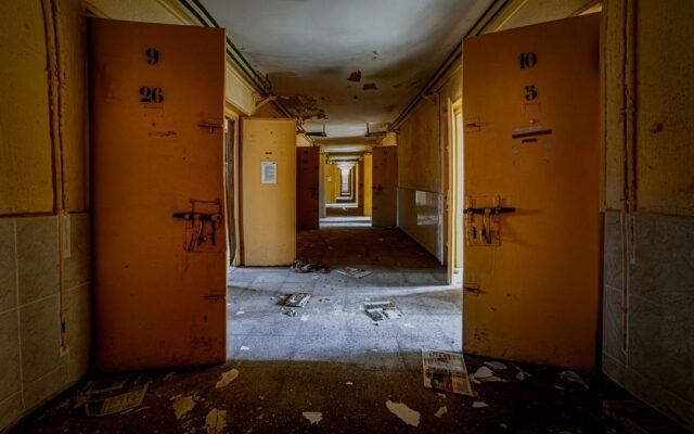 Порожній коридор покинутої будівлі з відчиненими металевими дверима й уламками на підлозі