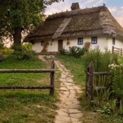 Біла українська хата під солом’яним дахом із кам’яною стежкою в золоту годину