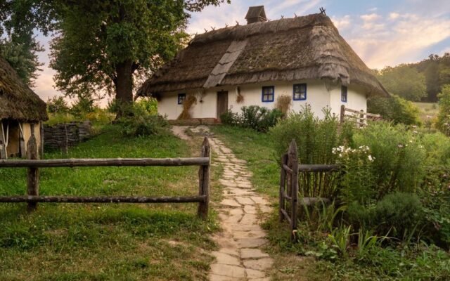 Біла українська хата під солом’яним дахом із кам’яною стежкою в золоту годину