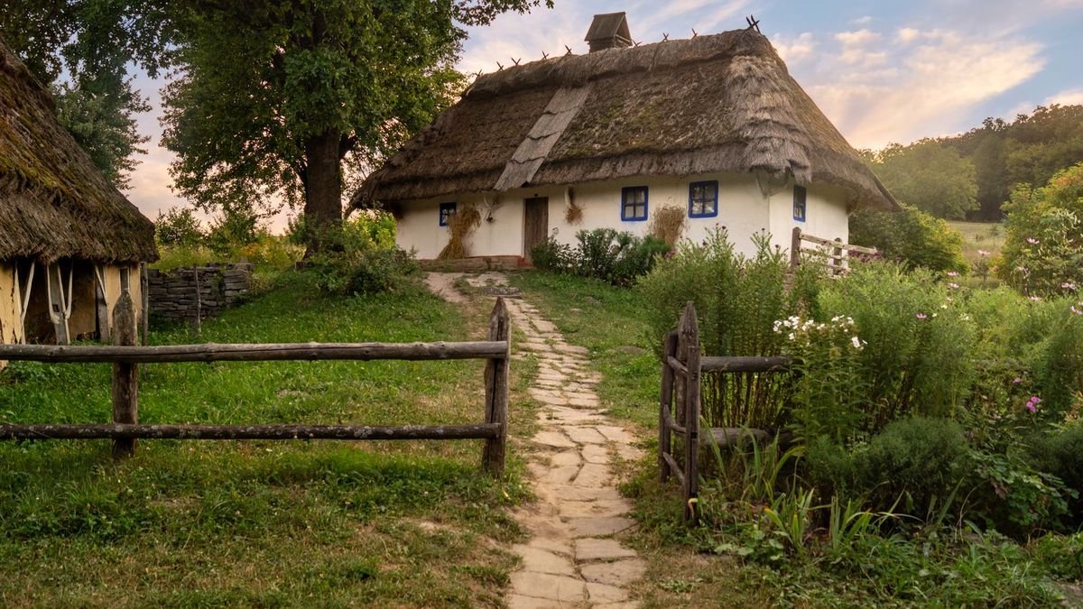 Біла українська хата під солом’яним дахом із кам’яною стежкою в золоту годину