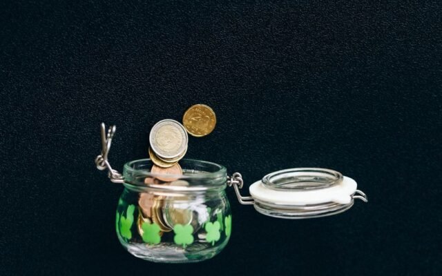 Монети падають у скляну баночку на темному тлі